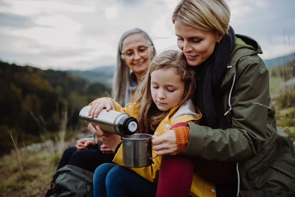 Kleines Mädchen mit Mutter und Großmutter, die oben auf dem Berg sitzen und heißen Tee einschenken. — Stockfoto