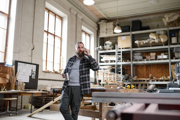 Feliz maduro carpinteiro masculino fazendo telefonema durante pausa para café em ambientes fechados na oficina de carpintaria. — Fotografia de Stock