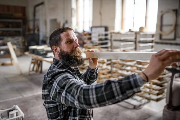 Зрелый плотник-мужчина, несущий деревянную доску в помещении столярной мастерской. Концепция малого бизнеса. — стоковое фото