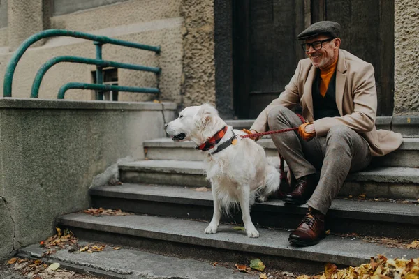 Happy senior man sitting on stairs and resting during dog walk outdoors in city. — Stockfoto