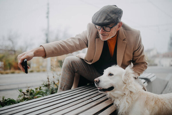 Happy senior man sitting on bench and taking selfie during dog walk outdoors in city. — Stock Photo, Image
