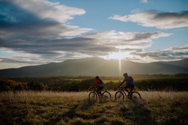 Active senior couple riding bikes outdoors in autumn nature at dusk.