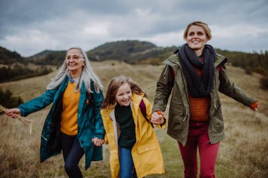 Happy small girl with mother and grandmother hiking outoors in autumn nature.