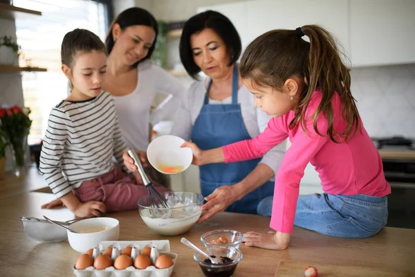 Szczęśliwe małe dziewczynki z matką i babcią co naleśniki mieszanki wewnątrz w domu, gotowanie. — Zdjęcie stockowe