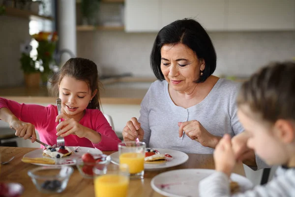 Chicas pequeñas felices con la abuela comiendo panqueques en casa, almorzando. —  Fotos de Stock