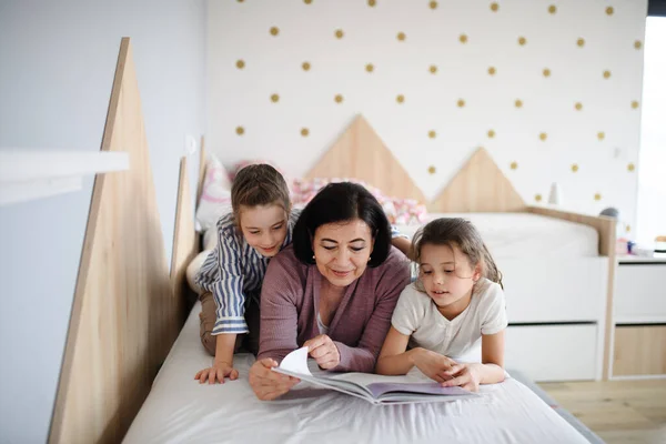 Meninas pequenas felizes com avó sênior em casa no quarto, lendo na cama. — Fotografia de Stock