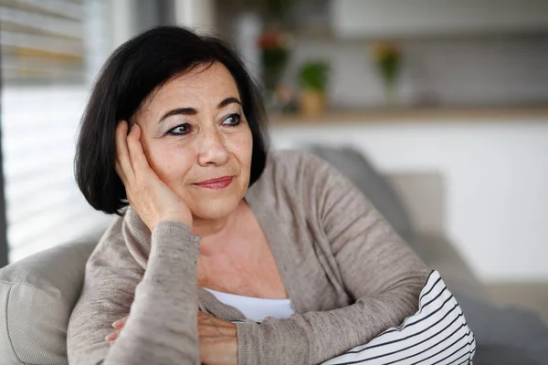 Close up of happy senior woman sitting on sofa and looking away indoors at home. — Zdjęcie stockowe