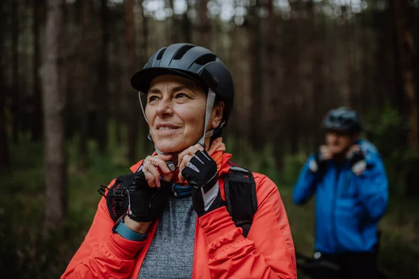 Senior couple bikers putting on cycling helmet outdoors in forest in autumn day. — Stock Photo, Image