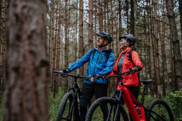 Pareja de ciclistas mayores con bicicletas eléctricas que admiran la naturaleza al aire libre en el bosque en el día de otoño. — Foto de Stock