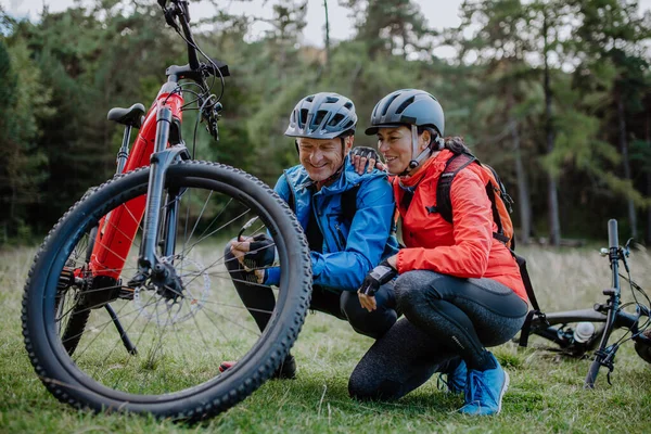 Coppia anziana attiva che ripara la bicicletta all'aperto nella foresta in autunno giorno. — Foto Stock