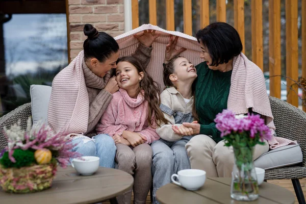 Deux sœurs heureuses avec mère et grand-mère assises enveloppées dans une couverture à l'extérieur dans un patio en automne — Photo