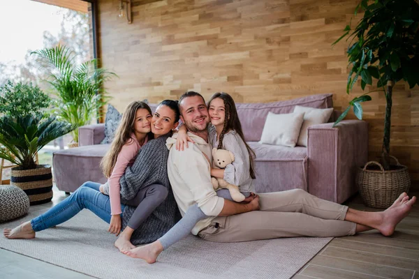 Two happy sisters with mother and father sitting on floor hugging and looking at camera at home — Φωτογραφία Αρχείου