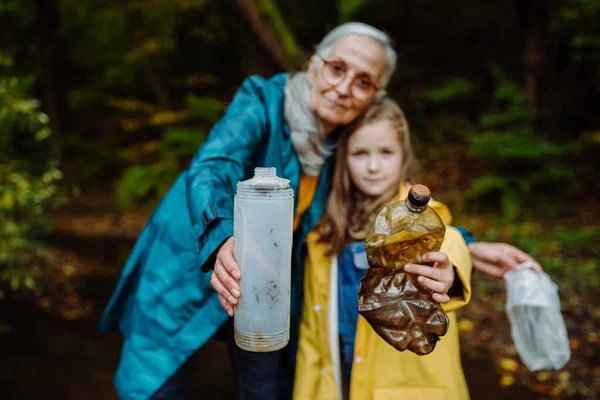 Klein meisje met oma tonen plastic afval wat ze vonden outoors in het bos. — Stockfoto