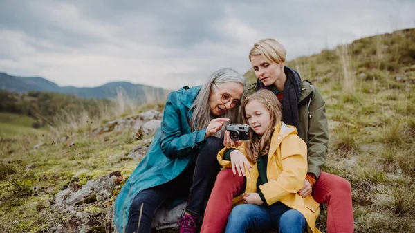 Small girl with mother and grandmother taking pictures on top of mountain in autumn day. — стоковое фото