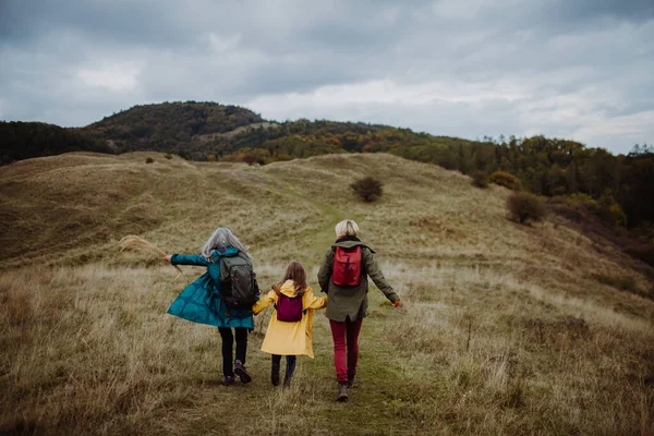 Rear view of small girl with mother and grandmother hiking outoors in autumn nature. — Stok fotoğraf