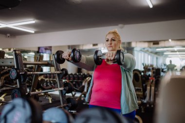 Ayrıca beden eğitimi alan ve spor salonunda dambılları kaldıran bir kadın.