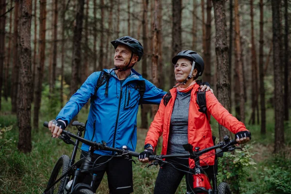 Seniorenpaar radelt mit E-Bikes im Herbst durch die Natur im Wald. — Stockfoto