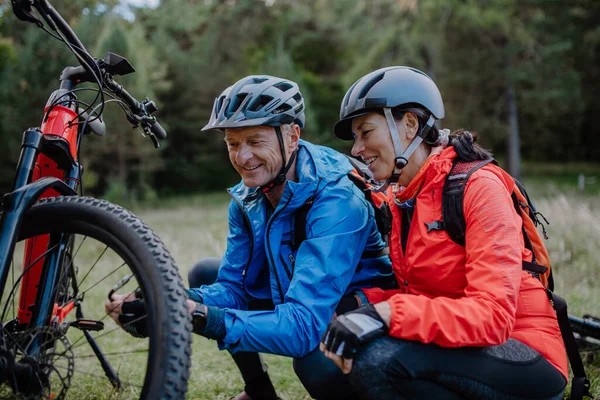 Pareja mayor activa reparando bicicleta al aire libre en el bosque en el día de otoño. — Foto de Stock