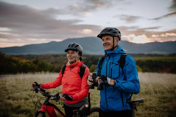 Senior par cyklister med kikare beundrar naturen utomhus på ängen på höstdagen. — Stockfoto