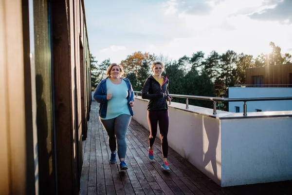 Overgewicht vrouw hardlopen en trainen met personal trainer buiten op het terras van de sportschool. — Stockfoto