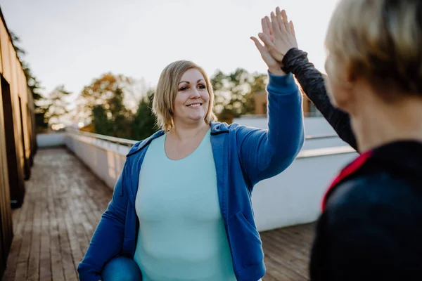 Glückliche übergewichtige Frau High Fiving mit Personal Trainer im Freien auf der Fitnessterrasse. — Stockfoto