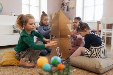 Yaratıcı sanat ve zanaat sınıfında karton ağaç boyayan bir grup küçük kız.