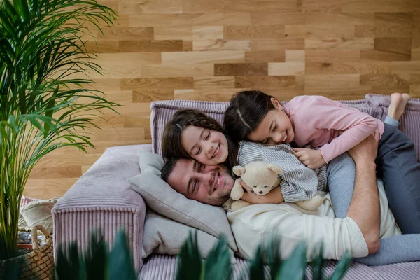 Két boldog nővér szórakozik apával, otthon heverésznek a kanapén.. — Stock Fotó