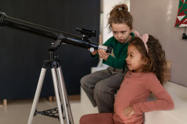 Zwei kleine Mädchen schauen zu Hause durchs Teleskop. — Stockfoto