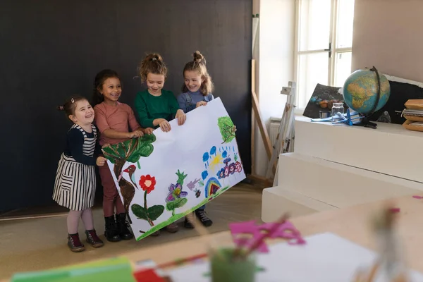 Группа маленьких девочек, держащих картину, которую они нарисовали во время занятий творчеством и ремеслом в школе — стоковое фото