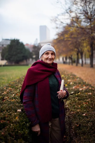 Mulher sênior feliz com livro sobre caminhada no parque da cidade no outono, olhando para a câmera. — Fotografia de Stock