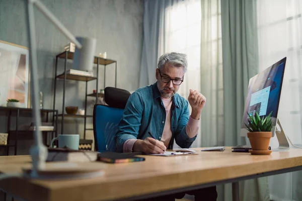 Volwassen man architect werkt op de computer aan het bureau binnen in het kantoor. — Stockfoto