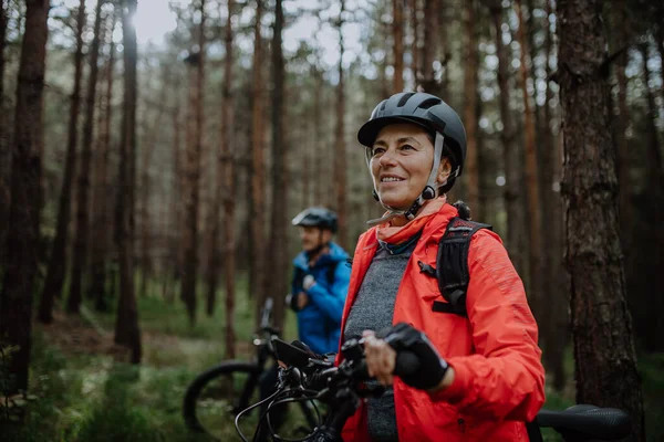 Pareja de ciclistas mayores con bicicletas eléctricas que admiran la naturaleza al aire libre en el bosque en el día de otoño. — Foto de Stock