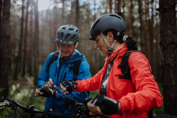 Pareja de ciclistas mayores estableciendo smartwatch al aire libre en el bosque en el día de otoño. — Foto de Stock