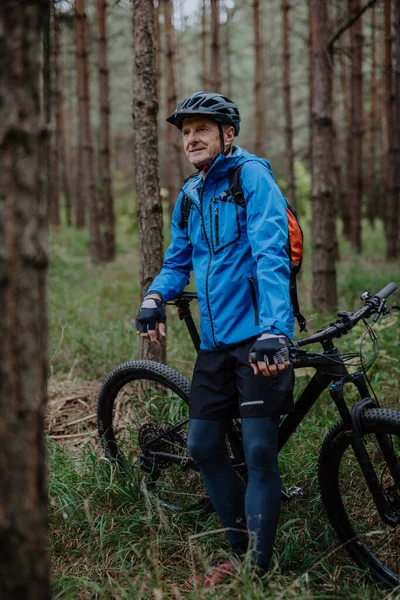 Aktiv senior man cyklist stående med cykel utomhus i skogen i höst dag. — Stockfoto