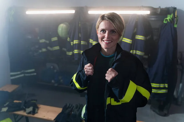 Щасливий серед дорослих жіночий пожежник дивиться на камеру в приміщенні пожежної станції вночі . — стокове фото