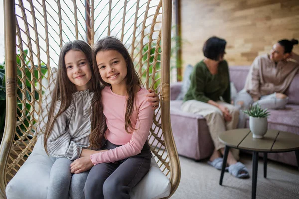 Irmãzinhas felizes sentadas em vime rattan pendurar cadeira dentro de casa no conservatório. — Fotografia de Stock