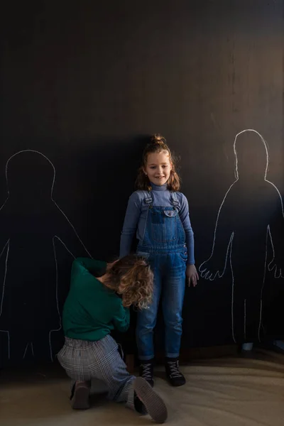 Rückansicht eines kleinen Mädchens, das seine Freunde mit Kreide an der Wand der Tafel im Spielzimmer zeichnet. — Stockfoto