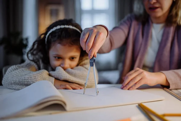 Madre aiutare la figlia con i compiti, disegnando un cerchio con le comasse in serata a casa. — Foto Stock