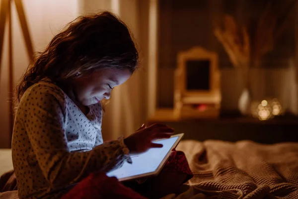 Felice bambina multirazziale utilizzando tablet sul letto in serata a casa. — Foto Stock