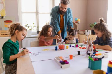 Yaratıcı sanat ve zanaat dersi sırasında öğretmenle proje üzerinde çalışan bir grup küçük çocuk..