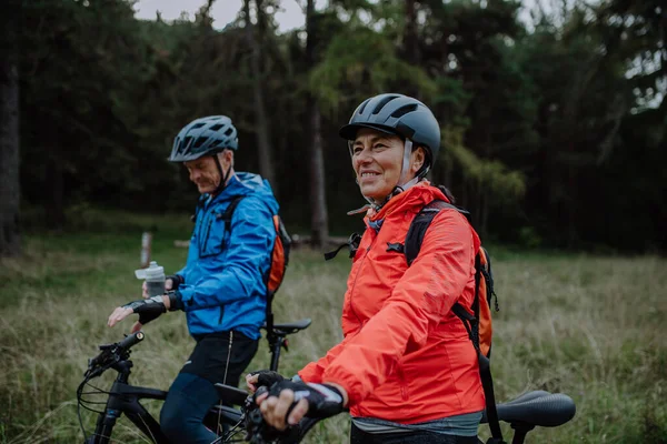 Seniorenpaar radelt mit E-Bikes im Herbst durch die Natur im Wald. — Stockfoto