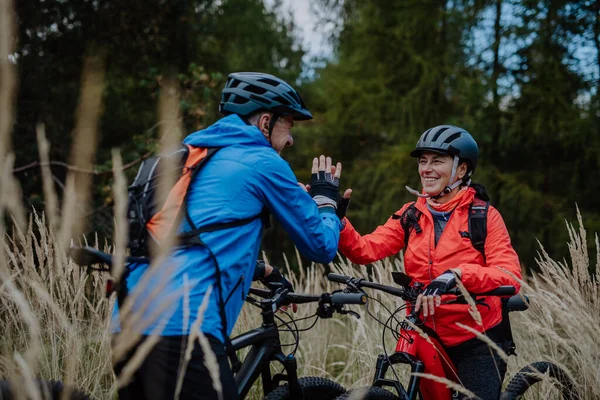 Senior pár bikers high fiving outdoors in forest in autumn day. — Stock fotografie