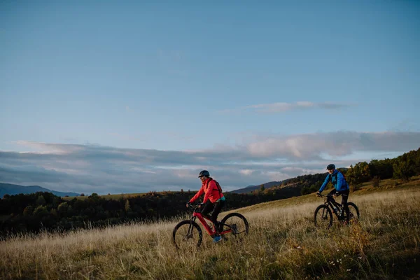 Vista lateral de pareja mayor activa montando bicicletas al aire libre en el campo en el día de otoño. —  Fotos de Stock