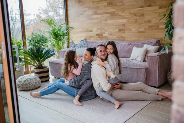 Dos hermanas felices con madre y padre sentados en el suelo abrazando y mirando a la cámara en casa — Foto de Stock