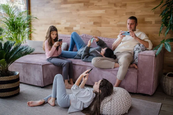 Familj med två små döttrar, alla använder mobiltelefon i vardagsrummet. — Stockfoto