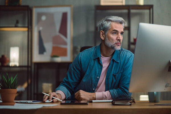 Mature man architect working on computer at desk indoors in office.