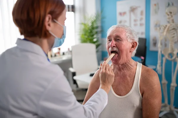 Kvinnlig läkare kontrollerar seniorer man hals på hennes kontor. — Stockfoto