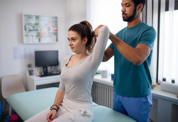 Fisioterapeuta masculino joven examinando a una paciente joven en una sala física —  Fotos de Stock