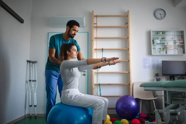 Fisioterapeuta masculino joven haciendo ejercicio con una paciente joven en una sala física —  Fotos de Stock