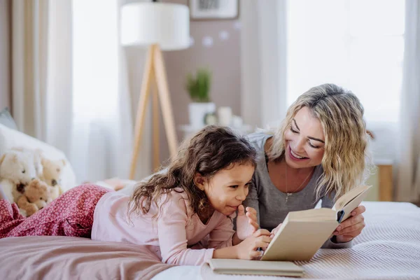 Felice madre con la sua figlioletta sdraiata sul letto e leggere libro a casa. — Foto Stock